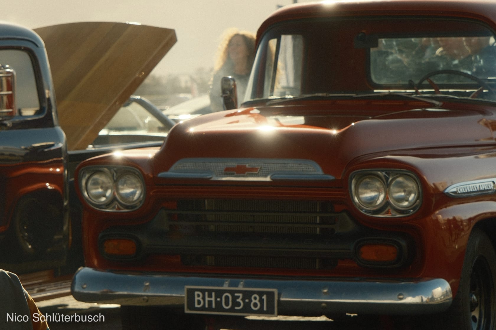 Roter Chevrolet Apache Pickup in der Frontansicht mit Chromgrill und Doppelscheinwerfern im Gegenlicht eines Oldtimertreffens