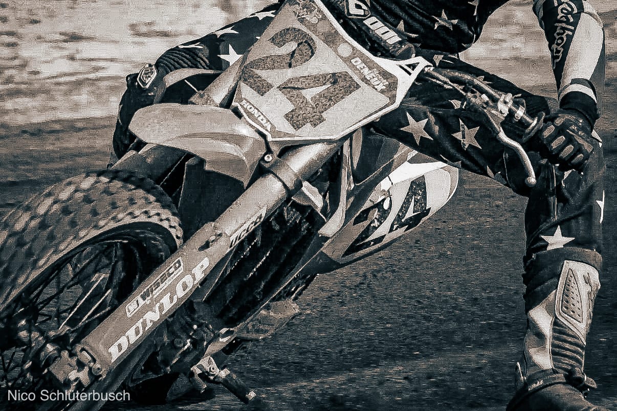 Motocross-Fahrer mit Startnummer 24 legt seine Honda in Schräglage, Nahaufnahme von Vorderrad, Gabel und ausgestrecktem Bein in Sepiatönen